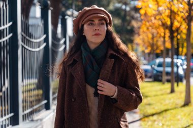 Güneşli bir şehirde sonbahar caddesinde şapkası ve paltosuyla yürüyen üzgün, genç beyaz bir kadın resmi. Psikoloji kavramı.
