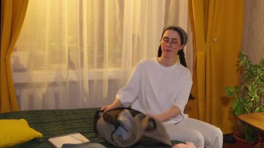 Bayan öğrenci, yaklaşan tatil yolculuğu için kıyafet ve aksesuarları katlayıp paketliyor. Orta çekim.