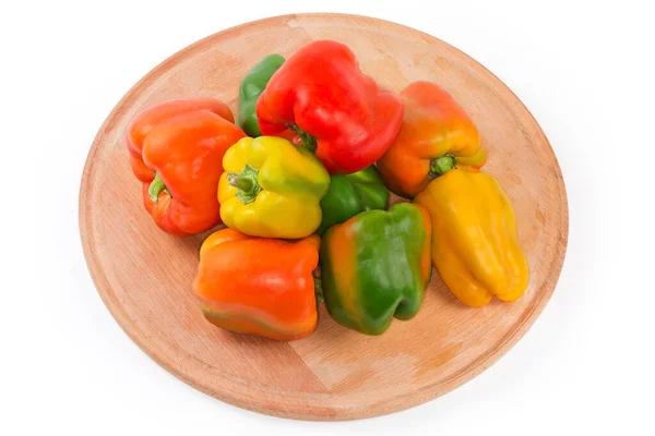 Stock image Several freshly harvested bell peppers different colors on the round wooden serving board on a white background