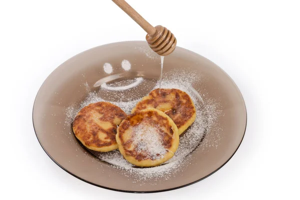 白い背景に木の蜂蜜のディップから注ぐ蜂蜜を添えて暗いガラス皿の上に揚げ小さな厚いチーズパンケーキ — ストック写真
