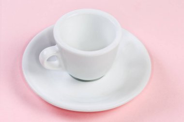 Espresso servisi için beyaz çay tabağının üzerinde bulunan küçük beyaz seramik kahve fincanı açık pembe bir yüzeye bakıyor.