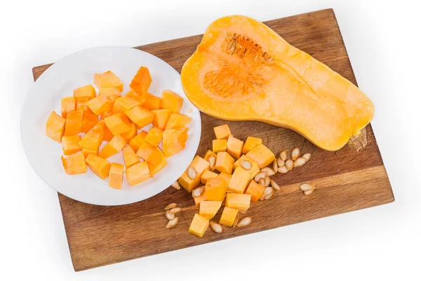 Diced slices of the butternut squash, seeds and half of the same squash cut lengthwise on the wooden cutting board, top view on a white background