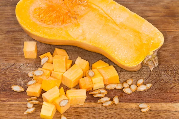 Diced slices of the butternut squash, seeds and half of the same squash cut lengthwise on the wooden cutting board, fragment close-up