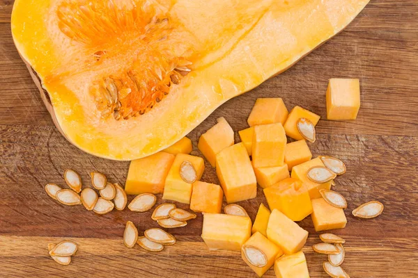 Diced slices of the butternut squash, seeds and half of the same squash cut lengthwise on the wooden cutting board, fragment top view close-up