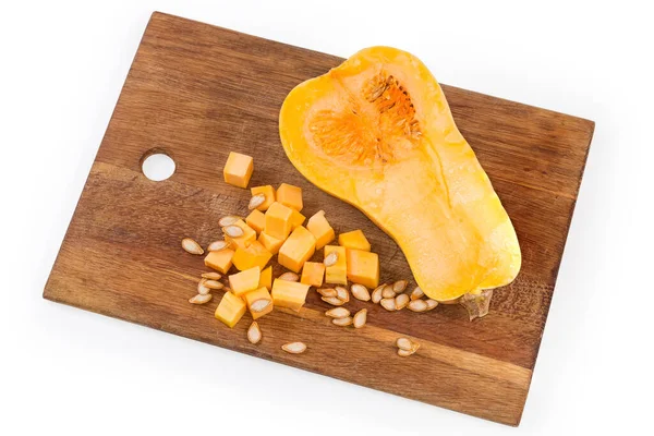 Diced slices of the butternut squash, seeds and half of the same squash cut lengthwise on the wooden cutting board, top view on a white background