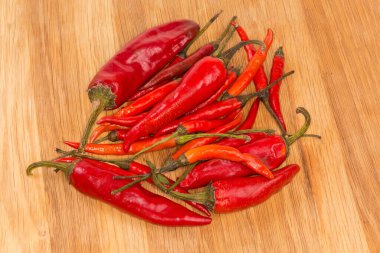 Ahşap bir yüzey üzerinde kurumuş kırmızı biberli küçük ve büyük kırmızı biber yığınları.