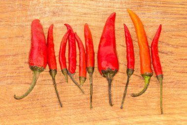 Küçük, ince ve büyük, kurutulmuş kırmızı biber kapsülleri ahşap kesim tahtasına dizilmiş.