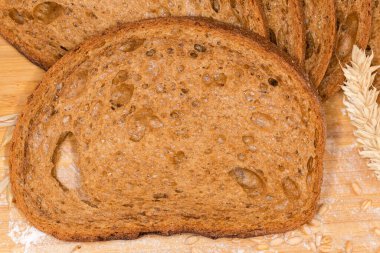 Çavdar ekmeğinden yapılan koyu kahverengi ekmek dilimi ve kulaklar arasında buğday unu ve kalan ekmeğe un serpiştirilmiş buğday taneleri.