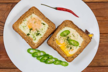 Kızarmış yumurtadan yapılmış iki açık sandviç. Güneşli tarafı yukarıda ve ekmek ekmeği ekmeği kırsal masada beyaz bir tabakta.