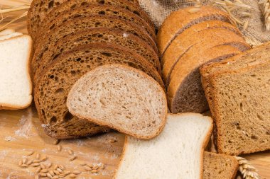 Kızartma için dilimlenmemiş beyaz ve tam tahıllı ekmek ve kulaklar arasında diğer kahverengi ekmek ve seçici bir odak noktasında un ile saçılmış kesme tahtasının üzerindeki tahıl