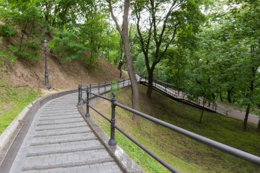 Curved path paved with stone slabs and with metal railings on the slope of hill in summer city park 