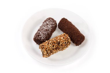 Three small soft chocolate cakes from biscuit crumbs and butter cream with sprinkling of cocoa powder, crushed nuts and sugar on a dish on a white background