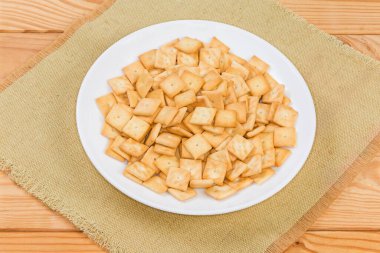 Small salty crackers of square shape on the white dish on the rustic table