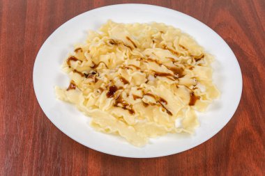Portion of boiled short noodles in the form of ribbons with ruffled sides poured on with sour sweet sauce on dish on the red wooden table