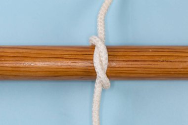 Rope simple overhand knot tied around a wooden pole, view on a blue background