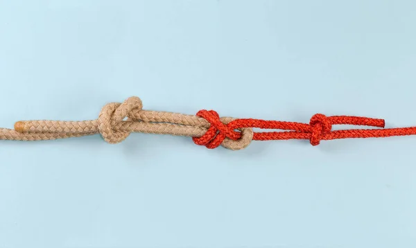 Tightened rope knot Duble sheet bend, intended to joining two ropes of different diameter or rigidity, with two stopper knots, view on a blue background