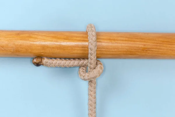 Rope knot Half hitch tied around a wooden pole, view close-up on a blue background