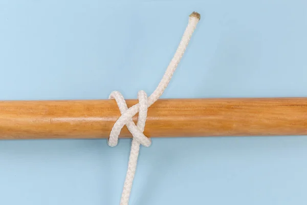 Rope knot Ground-line hitch used to attach a rope to an object tied around a wooden pole, view on a blue background