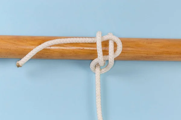 Rope knot Studding-sail bend used to attach a rope to to a cylindrical object, tied around a wooden pole, view on a blue background