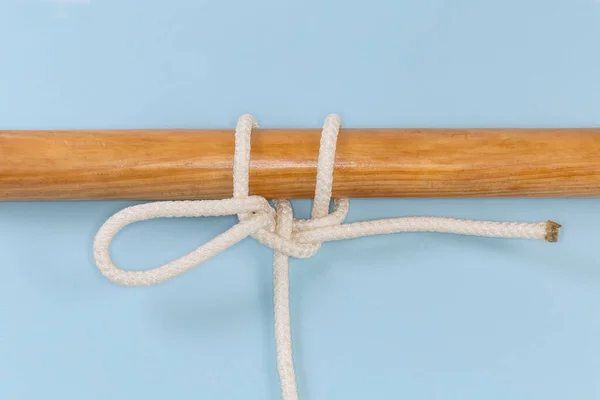 Rope Knot to lower a bucket, used to attach a rope to an object as a quick-release draw hitch tied around a wooden pole, view close-up on a blue background