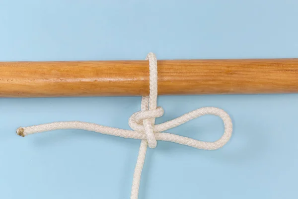 Rope knot Highpoint hitch, used to attach a rope to an object as a quick-release draw hitch tied around a wooden pole, view close-up on a blue background