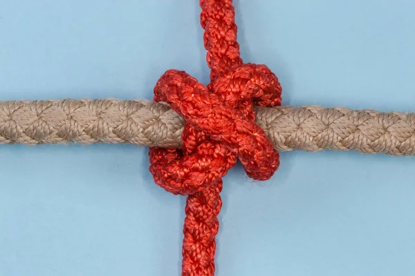 Tightened rope Constrictor knot, used to household binding, tied with an accessory cord around the thick rope, view close-up on a blue background