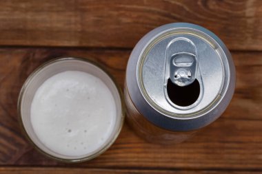 Open modern metal can from under the beer on a blurred background of beer glass and table, top view close-up in selective focus