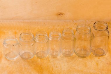 Various empty glass jars different sizes with screw thread on mouth for lids laid out in a row on a wooden surface