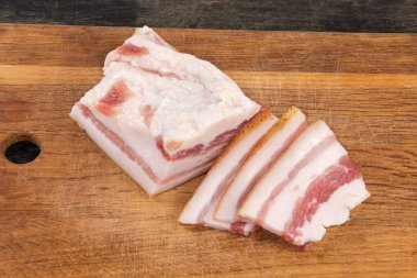 Partly sliced piece of the salted pork fatback on skin with meat layers on a wooden cutting board, close-up