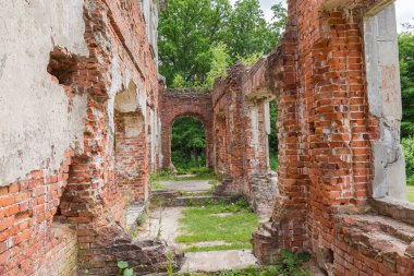 Scenic ruins of the old palace, partially destroyed walls of red brick of corridor with doorways and window holes against the forest