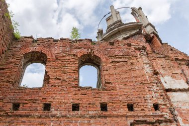 Scenic ruins of the old palace, partially destroyed wall with window holes of red brick and upper part of a tower against the cloudy sky