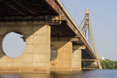 Modern road cable-stayed bridge over the wide river with one pylon and steel cables, bottom view from the water against the clear sky