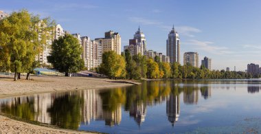 Modern housing estate with multistory buildings and trees on the banks of the river bay with reflecting in the water, panoramic view  in autumn morning