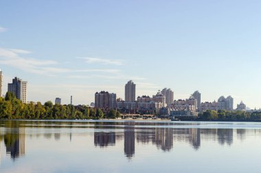 Modern housing estate with multistory buildings and trees on the riverbank with reflecting in the water in autumn morning
