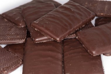 Heap of dark chocolate with filling in form of the small flat slices on a white background, fragment close-up in selective focus