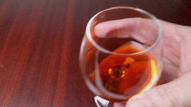 Shaking brandy in cognac glass above the wooden table