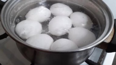 White chicken eggs during boiling in small stainless steel pot