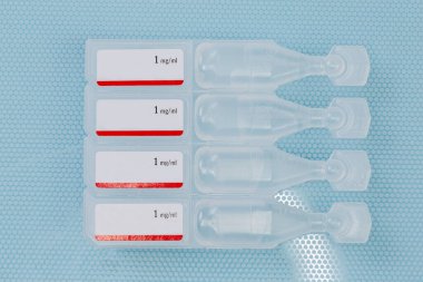 Göz damlaları küçük, tek kullanımlık plastik ampuller halinde damlalar halinde. Mavi bir yüzeye yakın çekim.