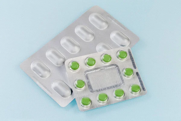 Foil blister pack with pills and blister pack with round green pills of the medication on the blue surface