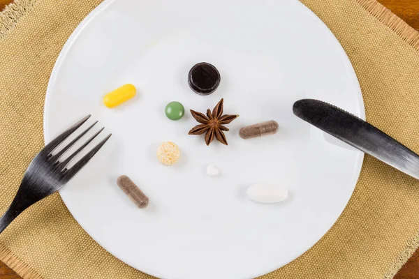 薬の錠剤とカプセルと異なる形状 サイズと色のサプリメント 木製のテーブルの上の場所マット上の刃物で白い皿の上に星のアニスフルーツ トップビュー — ストック写真