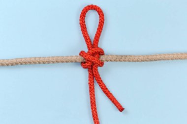 Sıkıştırılmış ip sıkıca bağlanmış kıskaçlı düğüm, kıskaç düğümünün kayması gibi, mavi arka planda kalın ipin etrafına bir aksesuar kablosu bağlanmış.