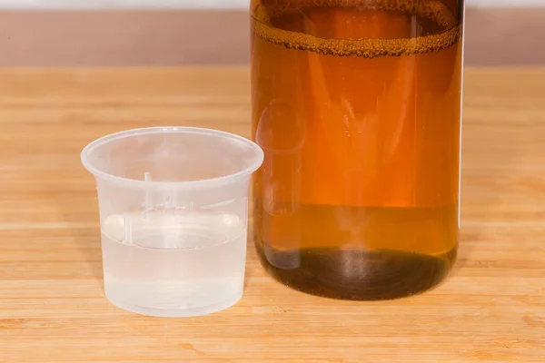 木製の表面に同じ薬と小さな茶色のガラス瓶の横にプラスチック製の測定カップの液体薬 — ストック写真