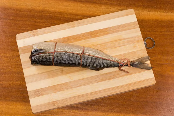 stock image Hot-smoked Atlantic mackerel without head, tied with twine for which fish was suspended in smoker, top view on a cutting board on a wooden table