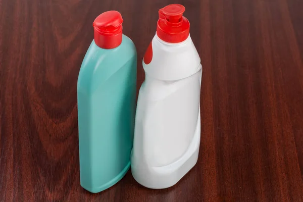 木製のテーブルの上に完全に閉じていない赤い蓋を持つ様々な家庭用洗浄剤の青緑と白のプラスチックボトル — ストック写真