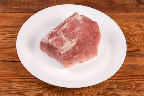 素朴なテーブルの上の白い皿の上の後ろ足から得られる新鮮な生の豚肉の大きな部分 — ストック写真