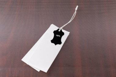 Dikdörtgen karton çarşaflar şeklinde iki boş beyaz elbise salıncak etiketi ve bir küçük siyah etiket. Üzerinde% 100 yazılı bir ip var. 