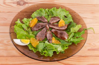 Haşlanmış ördek eti, yumurta, portakal dilimleri ve kırsal masadaki koyu cam tabakta farklı yeşilliklerden yapılmış salata.