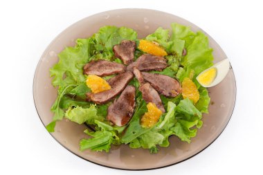 Kaynamış ördek eti, yumurta, portakal dilimleri ve beyaz arka planda koyu cam tabakta farklı yeşilliklerden yapılmış salata.