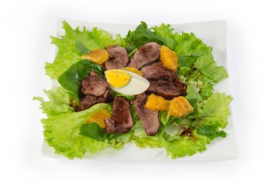 Kaynamış ördek eti, yumurta, portakal dilimleri ve beyaz arka planda kare bir tabakta farklı yeşilliklerden yapılmış salata.