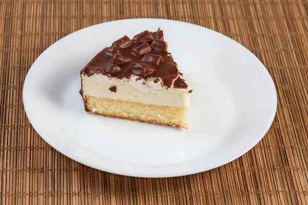 丸みを帯びたスポンジケーキのスライス 竹の場所マットの上に白い皿の上にマシュマロピースとチョコレートコーティング — ストック写真